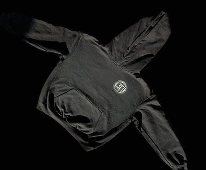 A black 3T branded over-sized hoodie with a front pouch and a hood, laid out on a textured surface.